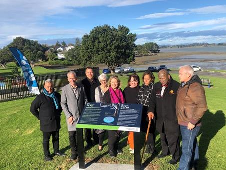 A group of Councillors, Local board members and iwi stand behind a new sign telling the story of Te Pua Keith Park's name. 