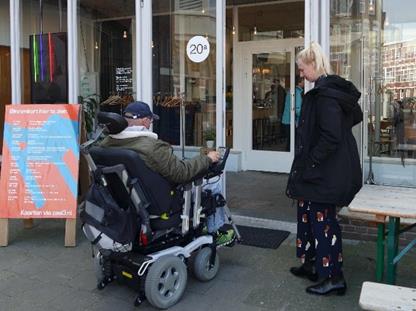 Man in wheelchair tests the accessibility of the doorstep of the Korzo theatre in the Hague. A female staff member stands next to him. 

Automatisch gegenereerde beschrijving