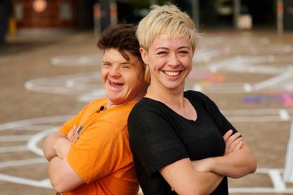Two artists stand back-to-back, with big smiles on their faces. Behind them is a large mural painted on the ground.