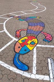 : A blue-tongued lizard painted on the ground, joining two spaces in the Snakes and Ladders game. The lizard is poking out a long blue tongue with a yellow stripe.