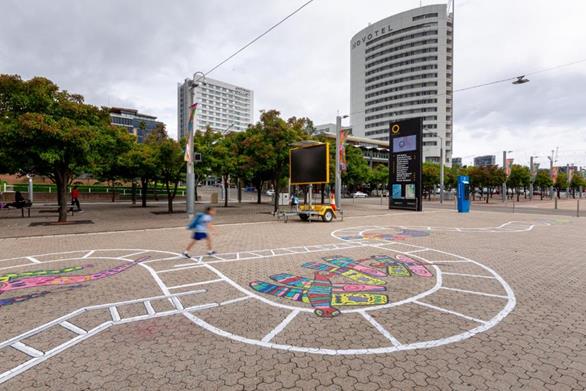 A detail of the Snakes and Ladders mural, painted on the ground. A child is walking along a painting of a ladder with crooked rungs.