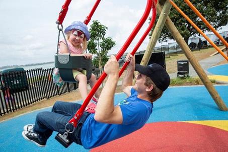 Father and toddler using a two-person swing, face-to-face. Toddler's face is brightly painted with face paint.